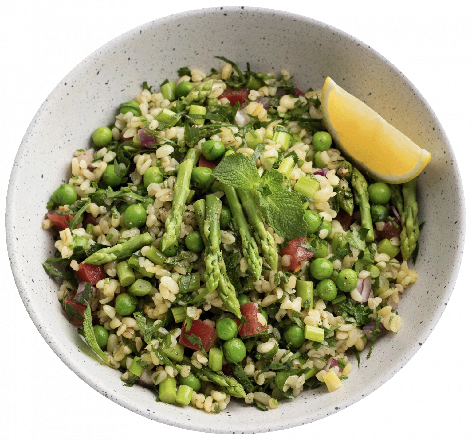 Insalata di farro e verdure servita in una ciotola chiara: contiene asparagi, piselli, pomodori, cipolla rossa, erbe fresche e uno spicchio di limone come guarnizione.
